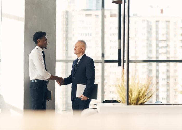 Senior recruiter with papers shaking hand of young Afro-American specialist while hiring him for work