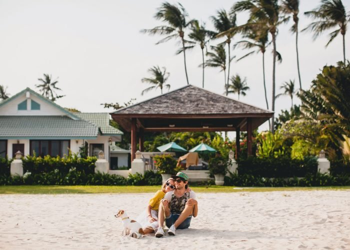 young stylish hipster couple in love walking playing dog puppy jack russell, tropical beach, cool outfit, romantic mood, having fun, sunny, man woman together, horizontal, vacation, house home villa